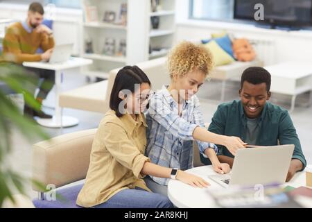 High angle view at multi-ethnic group of cheerful students using laptop together while working on project in library, copy space Stock Photo