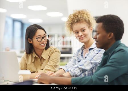 Multi-ethnic group of students using laptop together while discussing project in college library Stock Photo