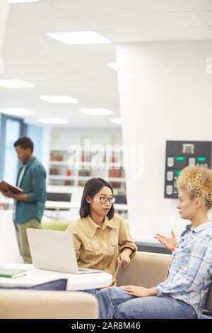 Portrait of two female students discussing project in college library, focus on Asian girl wearing glasses, copy space Stock Photo