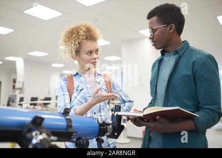 Waist up portrait of two students discussing astronomy project while standing by telescope in class or college library, copy space Stock Photo