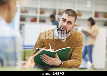 Portrait of bearded adult student talking to partner across table while discussing project in college library, copy space Stock Photo