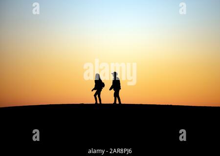 Two people silhouetted against twilight sky walk together in single file Stock Photo