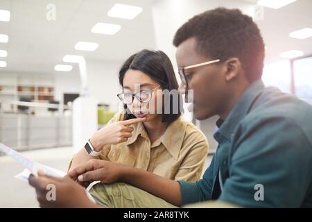 Couple of international students discussing papers while working on project in college library, copy space Stock Photo