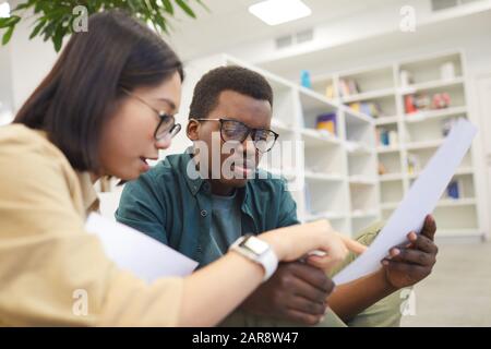 Two international students discussing papers while working on project in college library, copy space Stock Photo