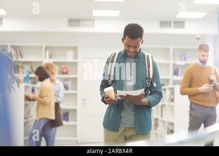 Waist up portrait of African-American student reading book while standing in college library, copy space Stock Photo