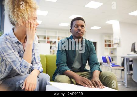 Portrait of young African-American man reading braille while studying with seeing friend in school library, copy space Stock Photo