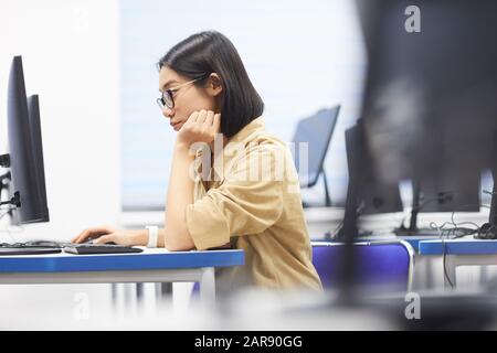 Side view portrait of young Asian woman using computer in class of college library, copy space Stock Photo