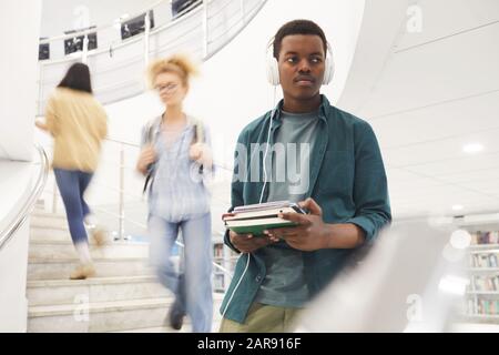 Waist up portrait of African-American student holding books while going down spiral stairs in modern college interior, copy space Stock Photo