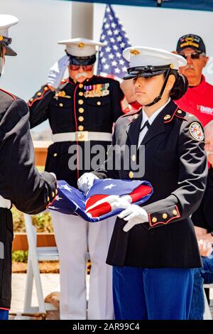 A Hispanic high school girl ROTC member assists in ceremonially folding a US flag at a July 4th observance as veterans salute in Newport Beach, CA.