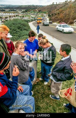 High school students smoke on the street outside their school after class in Aliso Viejo, CA. Note school bus in background. Stock Photo