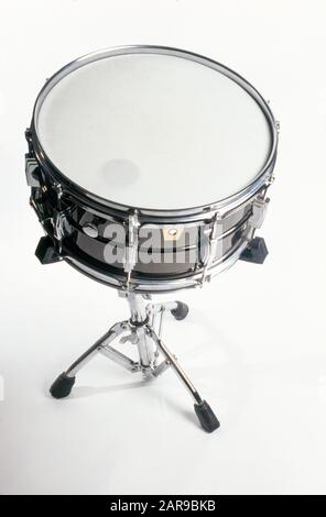 A snare drum or side drum is a percussion instrument that produces a sharp staccato sound when the head is struck with a drum stick, due to the use of a series of stiff wires held under tension against the lower skin. Snare drums are often used in orchestras[citation needed], concert bands, marching bands, parades, drumlines, drum corps, and more. It is one of the central pieces in a drum set, a collection of percussion instruments designed to be played by a seated drummer and used in many genres of music. Stock Photo