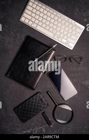 Flat lay office desktop work space of wireless keyboard, pen, phone, magnifying glass and black reading glasses on black background, top view, copy sp Stock Photo