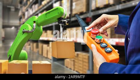 Industrial robot holding a box and worker operating a robot machine with a control panel on stock shelves background Stock Photo