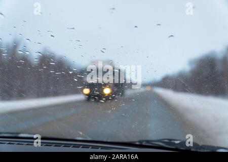 Blurred view through the windshield in the raindrops on the highway, which is moving towards a large car. Selective focus Stock Photo