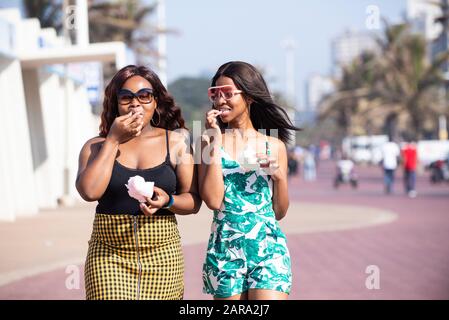 Two young women walking and eating candy floss. Stock Photo