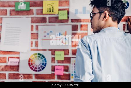 Asian man creative director designer looking at data chart and find idea on brickwall at modern office.brainstroming creative ideas concpet Stock Photo