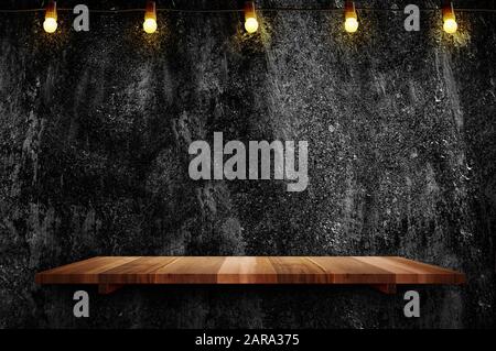 Empty brown plank wood shelf at black grung concerte wall background with light bulbs string,Mockup for display or montage of product or design Stock Photo
