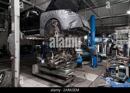 A used car raised on a lift for repair and under it a detached engine ...
