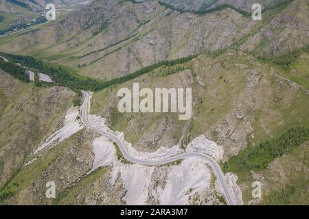 Aerial view of Serpentine Road Among Green Hills of Chike-Taman pass in Altai Mountains. Asphalt road going through cliff. Stock Photo