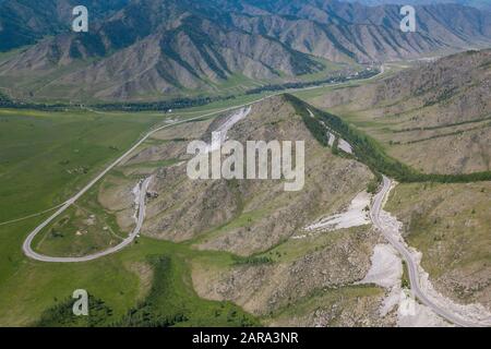 Aerial view of Serpentine Road Among Green Hills of Chike-Taman pass in Altai Mountains. Asphalt road going through cliff. Stock Photo