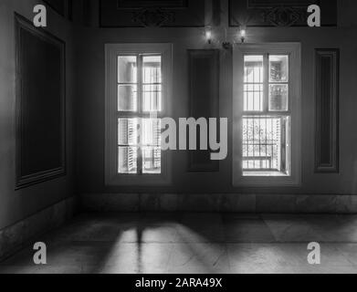 Black and white high contrast shot of two narrow windows, revealing strong light into dark room with white tiled marble floor  Stock Photo