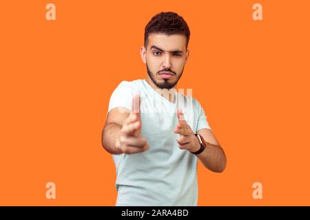 Gun gesture. Portrait of dangerous young brunette man with beard in casual white t-shirt pointing with finger pistols at camera, pretending to shoot. Stock Photo