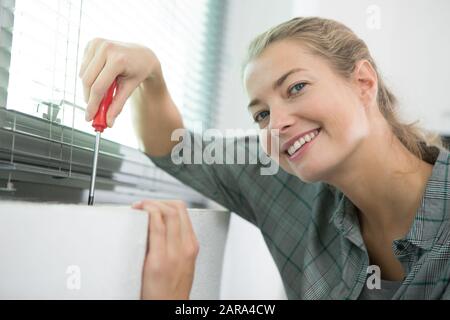 happy woman installing blinds with screwdriver Stock Photo