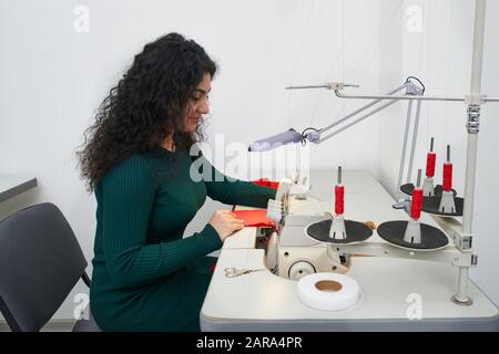 Young woman using professional overlock sewing machine in workshop. Equipment for edging, hemming or seaming clothes at tailors shop Stock Photo