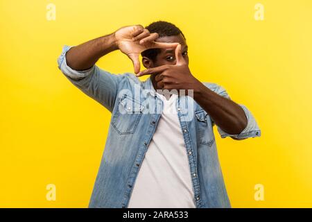 Portrait of focused curious man in denim casual shirt with rolled up sleeves looking through photo frame made of hands, viewing distant with interest. Stock Photo