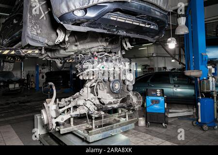 A used car raised on a lift for repair and under it a detached engine ...