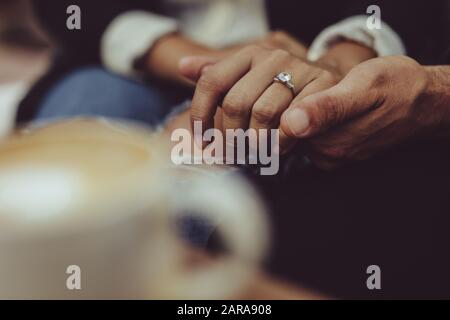 Close-up of couple holding hands at cafe together. Man holding hand woman wearing engagement ring. Stock Photo