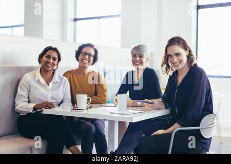 Four business women sitting at table and looking at camera. Team of female business professionals. Stock Photo