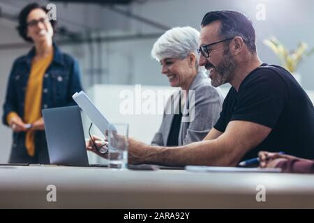 Businessman looking at some paperwork and smiling while sitting in a team meeting in office. Group of happy business man and woman during a meeting in Stock Photo