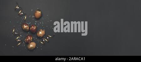 Golden eggs, multicolored shiny sequins, golden glitter serpentine on a dark background with place for text. Can be used for web banner, poster, voucher. Stock Photo