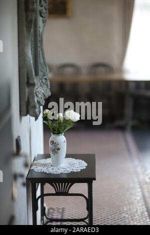 Porcelain vase with white peonies on a light wooden table under the mirror in the hallway Stock Photo