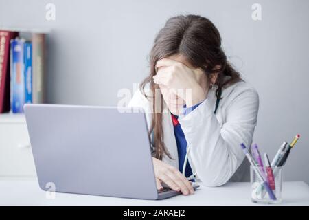 Tired Young Woman Doctor Working with a Laptop in a Clinic Stock Photo