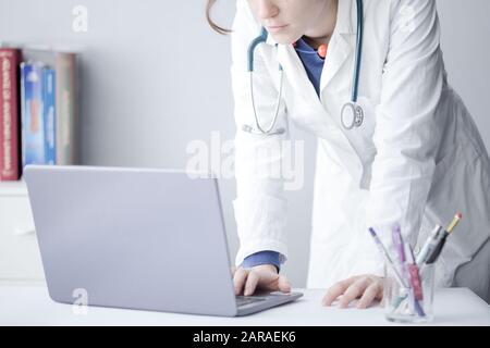 Standing Young Woman Doctor Working with a Laptop in a Clinic Stock Photo