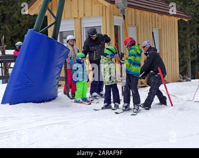 Children skiers get help by attendant on T-bar surface ski lift. Rogla ski resort, Slovenia. Stock Photo