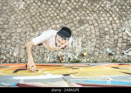 Young graffiti writer painting with color spray his picture on the wall - Top with of contemporary artists at work - Urban lifestyle,street illegal ar Stock Photo