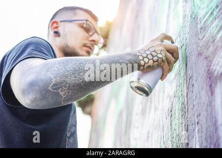 Tattooed graffiti artist painting with color aerosol on the wall - Contemporary spray write at work - Urban lifestyle,street art concept - Focus on hi Stock Photo