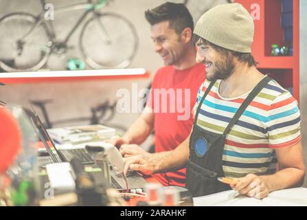 Two bicycle repairer colleagues working in bike garage - Positive mood bmx seller using computer in workshop  - Retail selling and sport trend concept Stock Photo