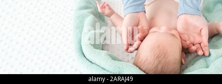 Baby face massage banner with copy space. Masseuse or mother gently stroking baby boy face with both hands. Close up cropped shot. Stock Photo