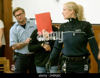 Dortmund, Germany. 27th Jan, 2020. The accused (M) is led in handcuffs into the courtroom of the regional court. Six months after a woman's body was found in a suitcase, the 24-year-old ex-partner of the victim is on trial. The public prosecutor's office accuses the man of having first strangled his former partner in the argument and then killed her with 76 stab wounds. Afterwards he is said to have stowed the body in a suitcase and parked it near an S-Bahn station. Credit: Bernd Thissen/dpa/Alamy Live News Stock Photo