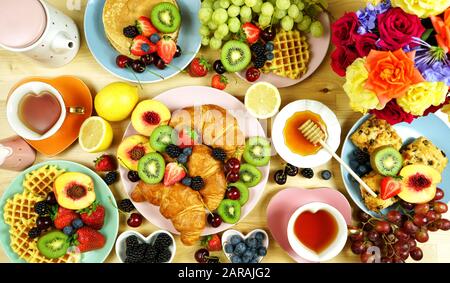 Indulgent breakfast creative layout flat lay with croissants, pancakes, waffles, fruit and roses. Top view. Stock Photo