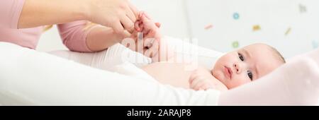 Baby massage banner. Mother gently massaging her baby boy while applying body lotion to his skin. Baby lying on back and looking at camera. Stock Photo