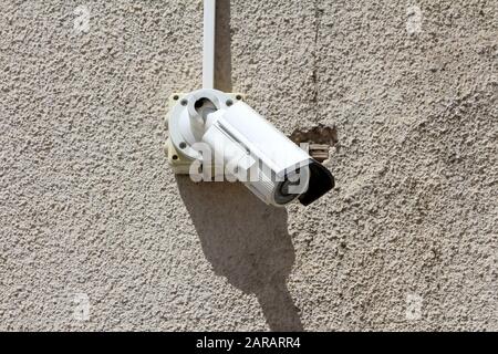 Freshly installed new small white closed circuit TV CCTV security camera mounted on wall of old abandoned building with cracked facade Stock Photo