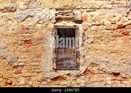 Narrow dilapidated small window opening covered with wire mesh on ruins of old red bricks suburban family house in old part of town Stock Photo
