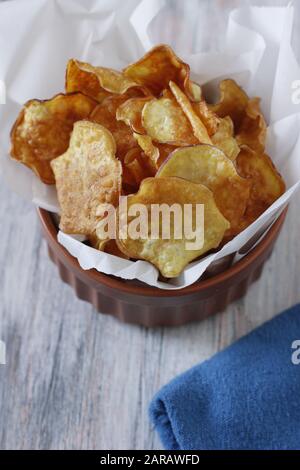 Light golden brown white sweet potato chips inside brown bow,l lined with white wax papper, on white and blue background with blue napkin Stock Photo