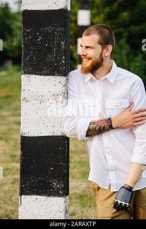 Cheerful bearded middle age man with bionic hand leaning on a striped post Stock Photo