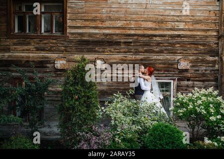 Passionate newly wed couple kissing lips in front of an old wooden house wall Stock Photo